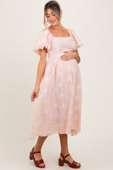 woman wearing a light pink puff sleeve maternity dress with floral patterns and holding her baby bump
