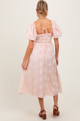 woman wearing a pink floral embroidered maternity dress with puff sleeves and a fitted bodice, showing her back