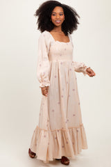 woman wearing a beige long sleeve floral embroidered maxi dress with smocked bodice and ruffle hem