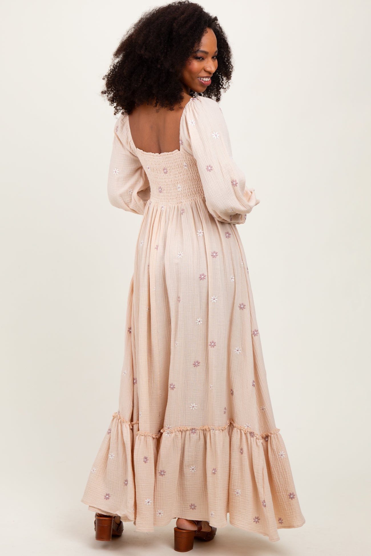woman wearing a light pink long sleeve maxi dress with floral embroidery and a tiered skirt, seen from the back