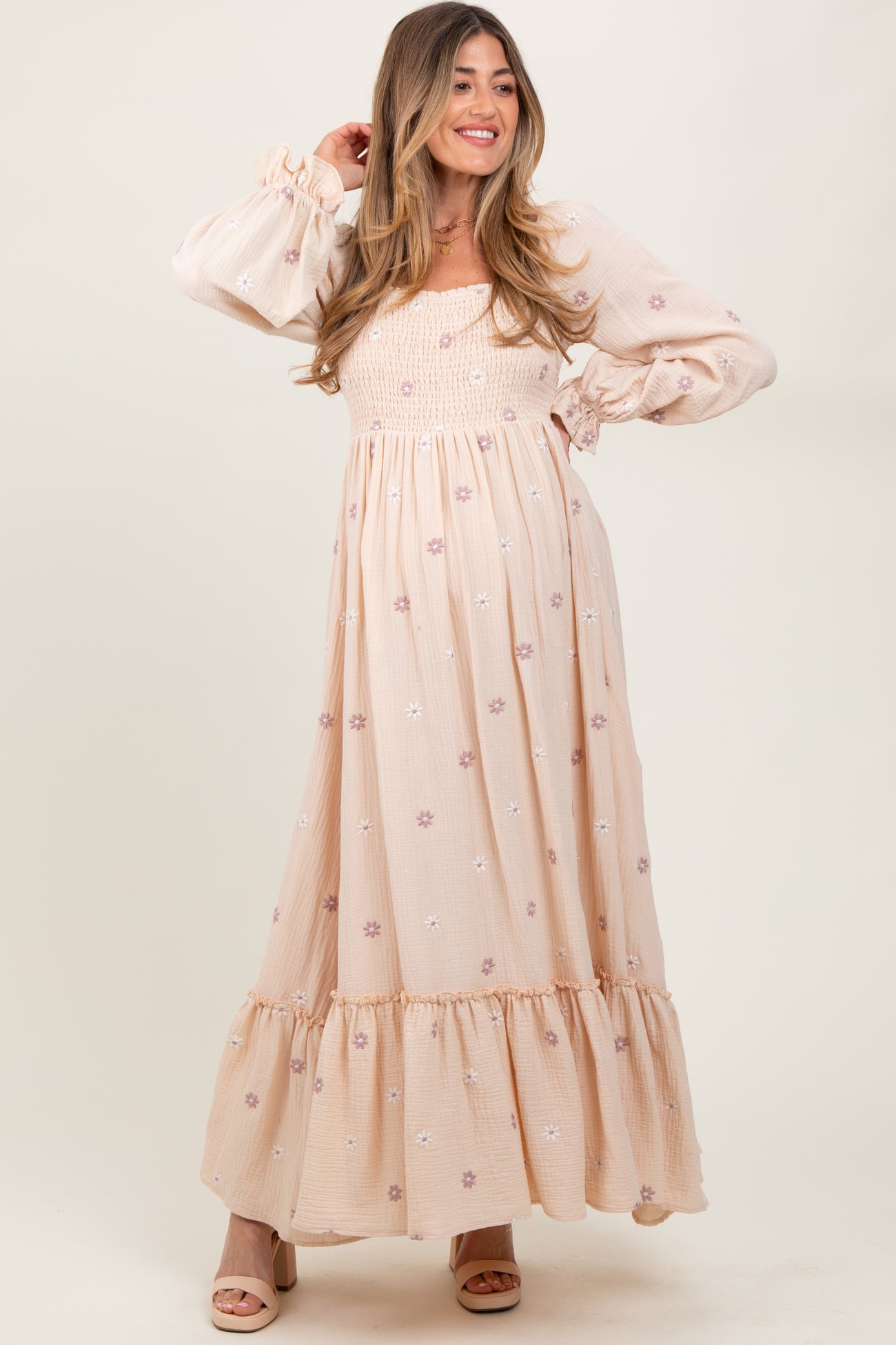 woman wearing a blush pink floral maternity maxi dress with puff sleeves and a smocked bodice, showcasing her baby bump