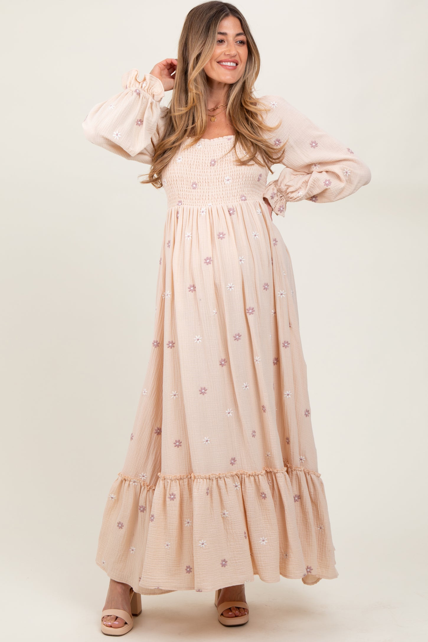 woman wearing a blush pink floral maternity maxi dress with puff sleeves and a smocked bodice, showcasing her baby bump