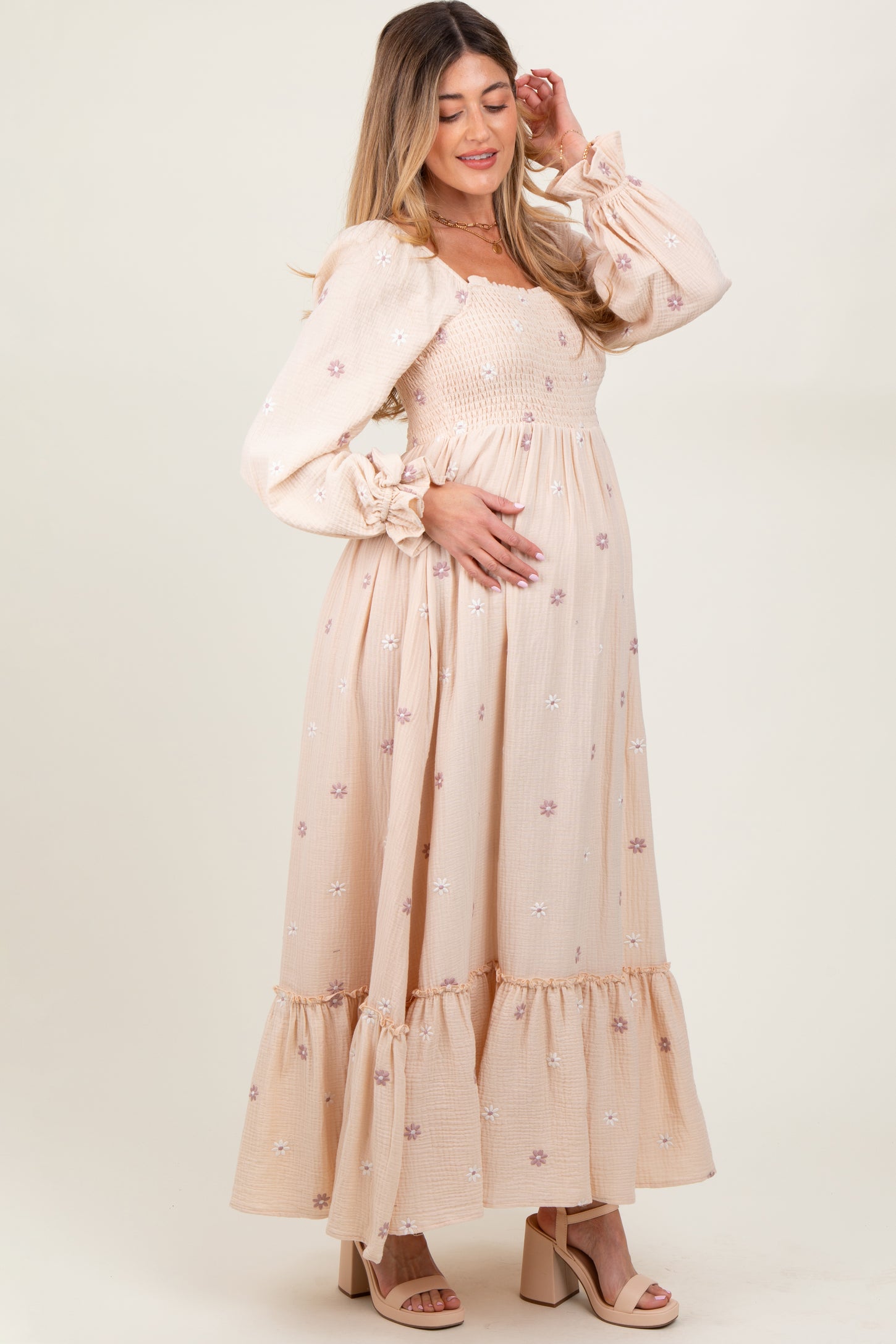 woman wearing a light beige maternity maxi dress with puff sleeves and floral embroidery, holding her baby bump