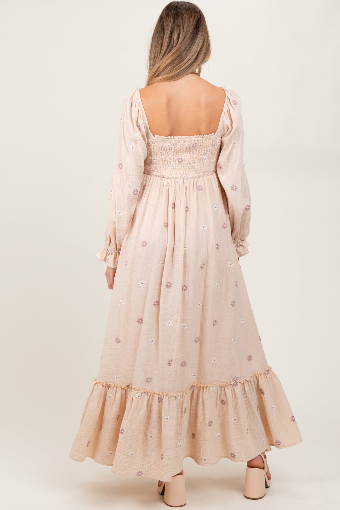 woman wearing a light pink maternity dress with floral embroidery and a ruffled hem, showing a baby bump from the back