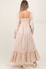 woman wearing a light pink maternity dress with floral embroidery and a ruffled hem, showing a baby bump from the back