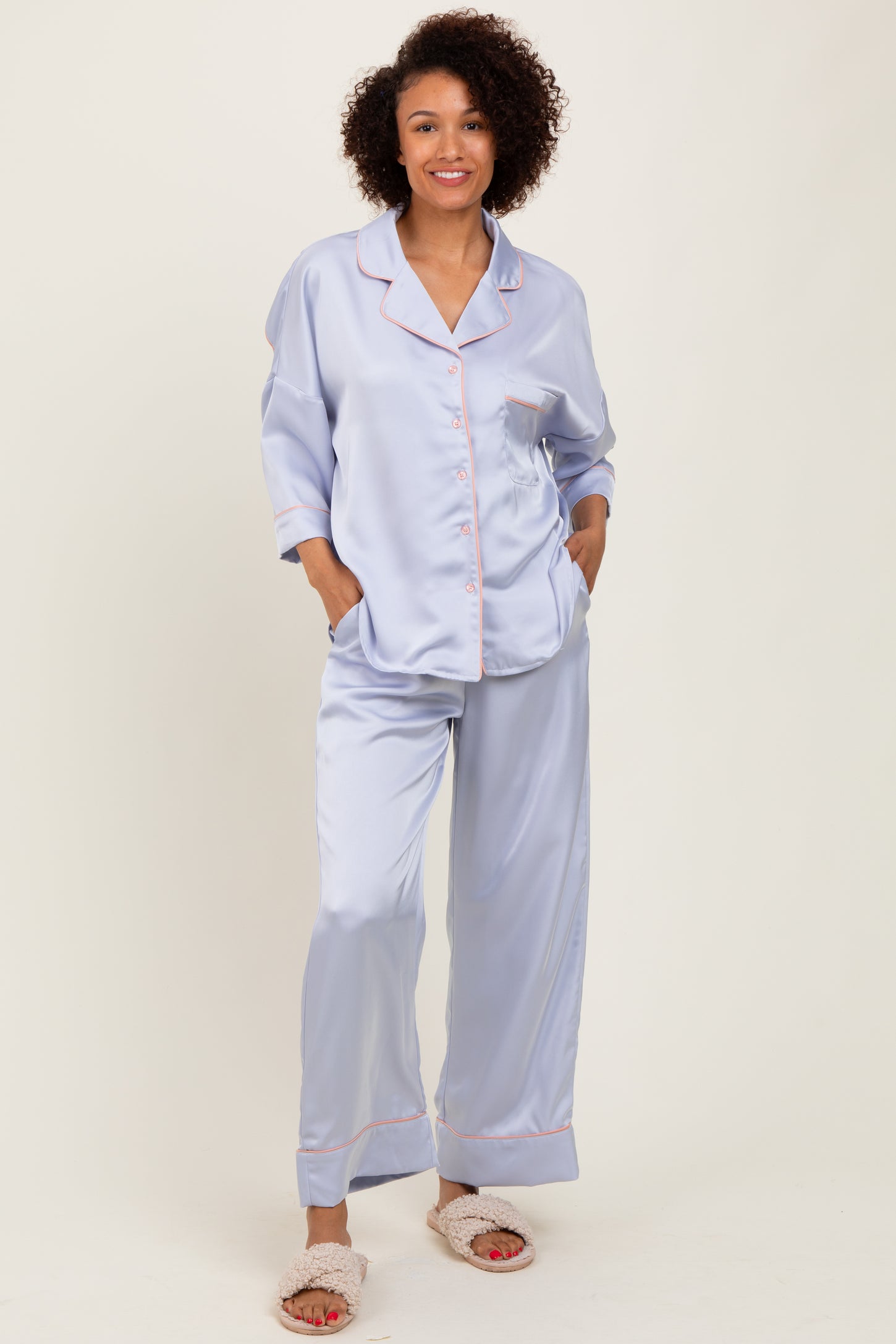 woman wearing a light lavender satin pajama set with contrasting pink piping and pockets