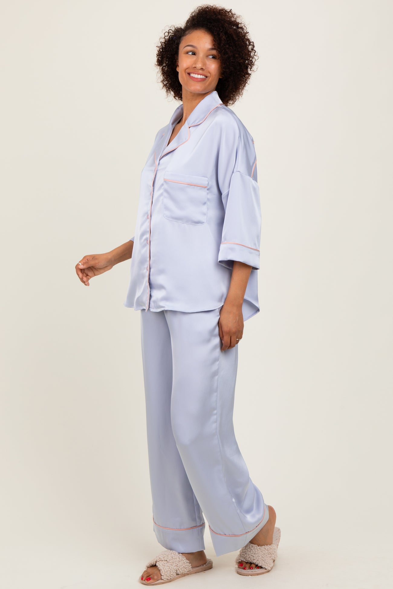woman wearing a light blue satin pajama set with short sleeves and piping details, styled with soft slippers