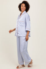woman wearing a light blue satin pajama set with short sleeves and piping details, styled with soft slippers