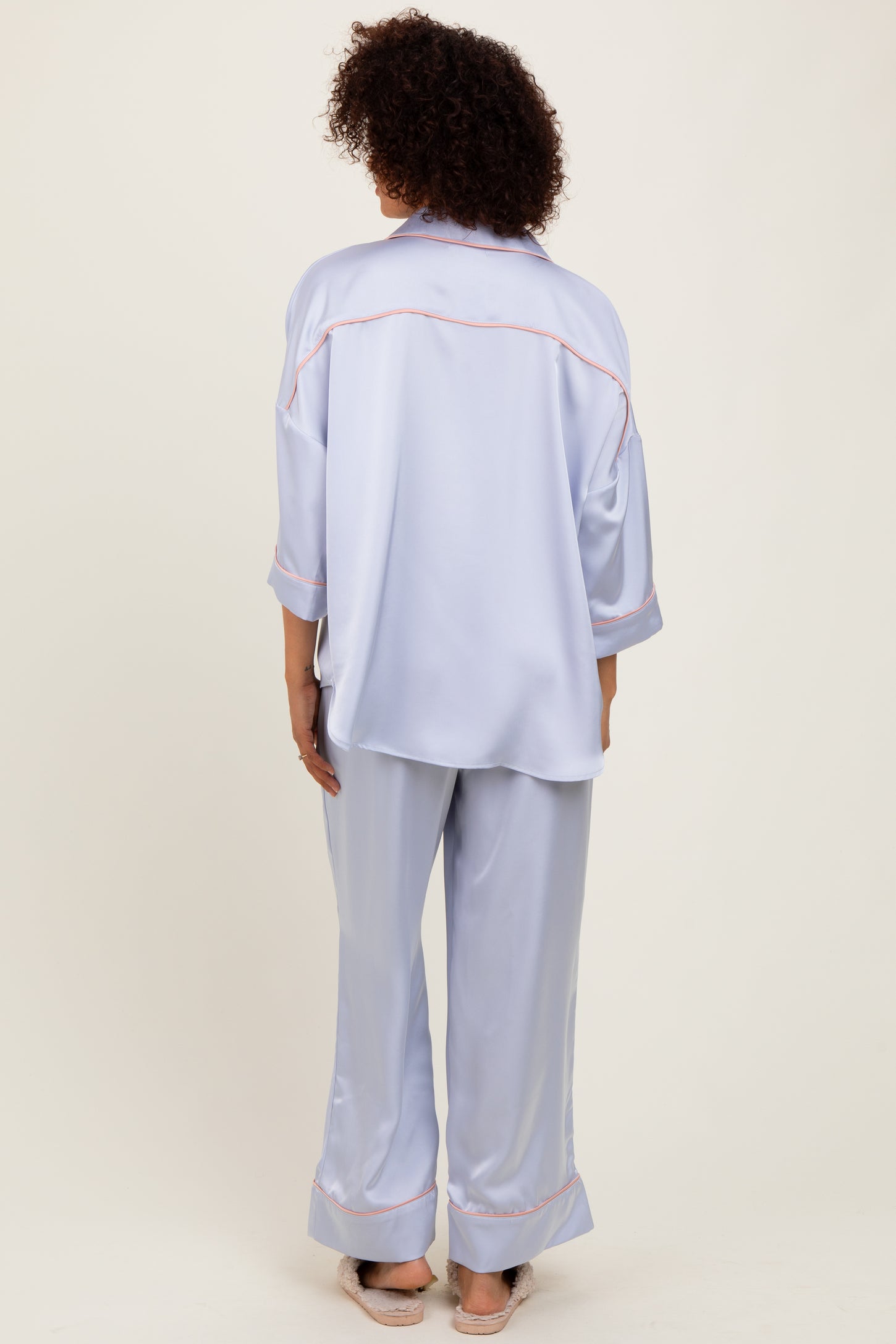 woman wearing a light blue satin pajama set with a loose fit and contrasting trim details, viewed from the back