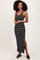 woman wearing a black and white striped sleeveless maxi dress with a side slit and black slide-on shoes