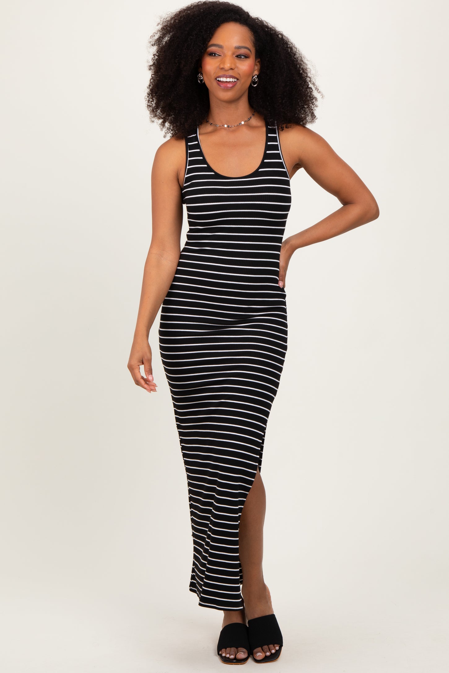 woman wearing a black and white striped sleeveless maxi dress with a side slit and open-toed black heeled sandals