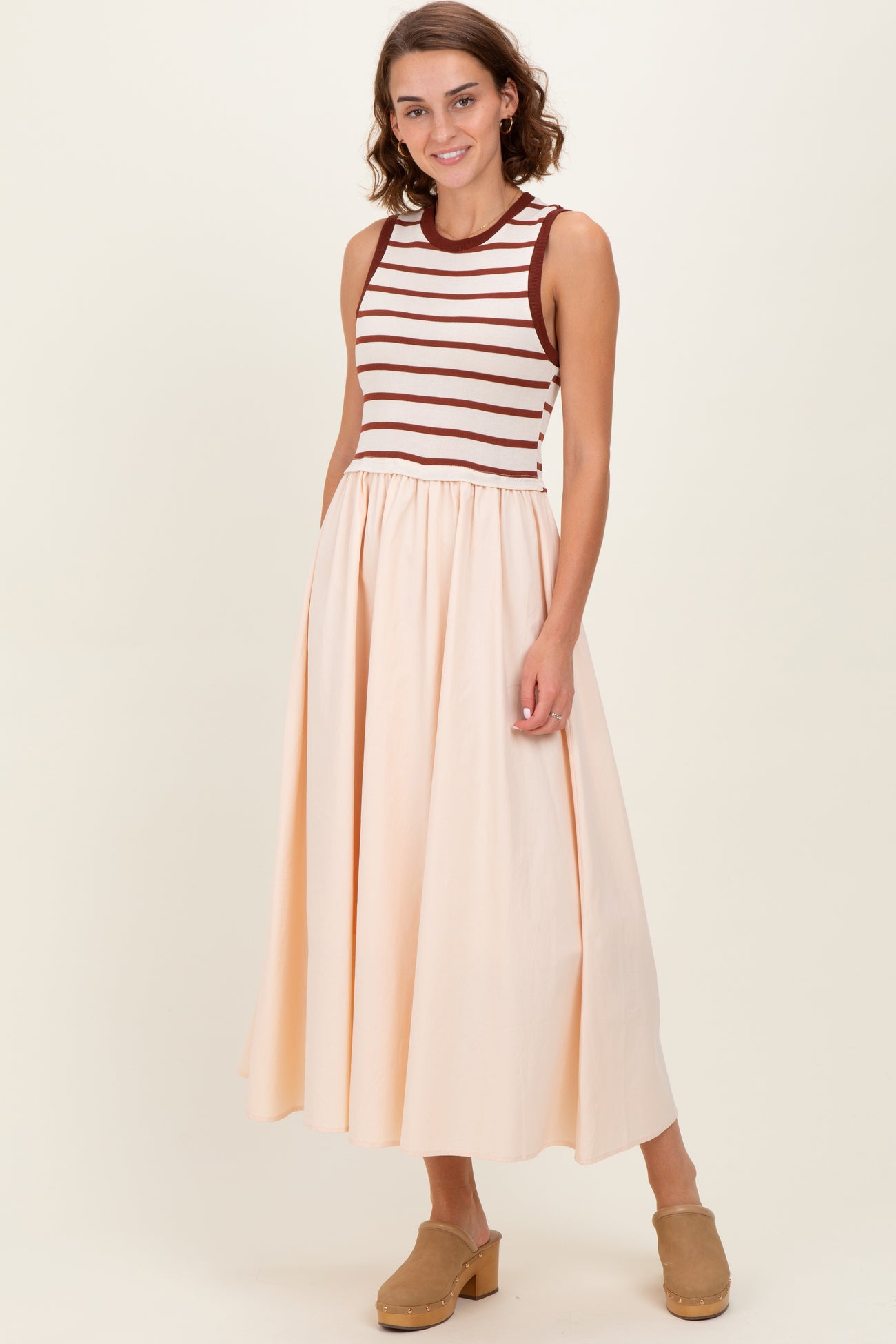 woman wearing a sleeveless striped bodice dress with a flowy peach skirt and brown clogs
