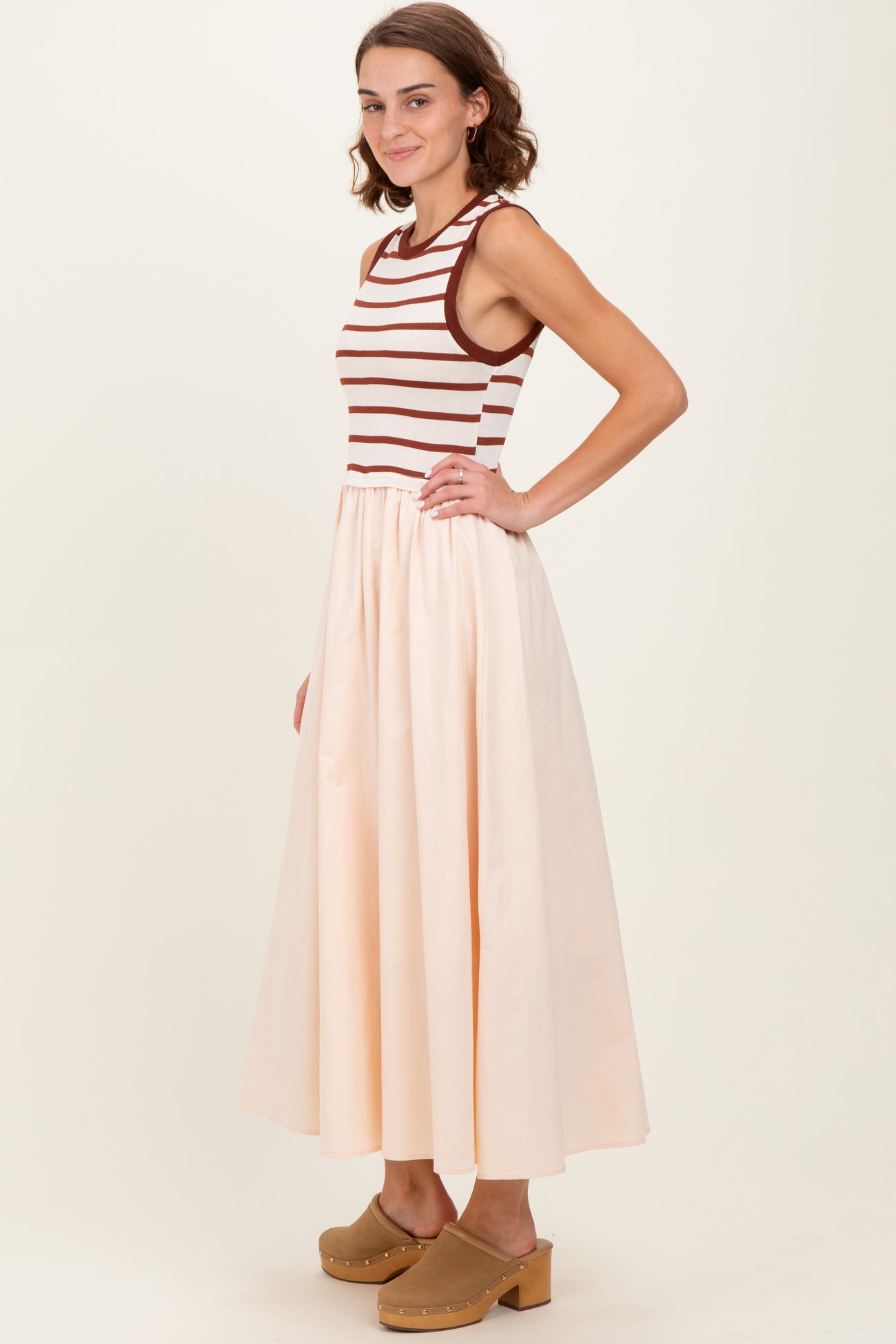 woman wearing a striped sleeveless top with a cream-colored maxi skirt and clogs, posed sideways