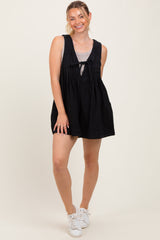 woman wearing a black sleeveless swing dress with a tie detail in the front and white sneakers