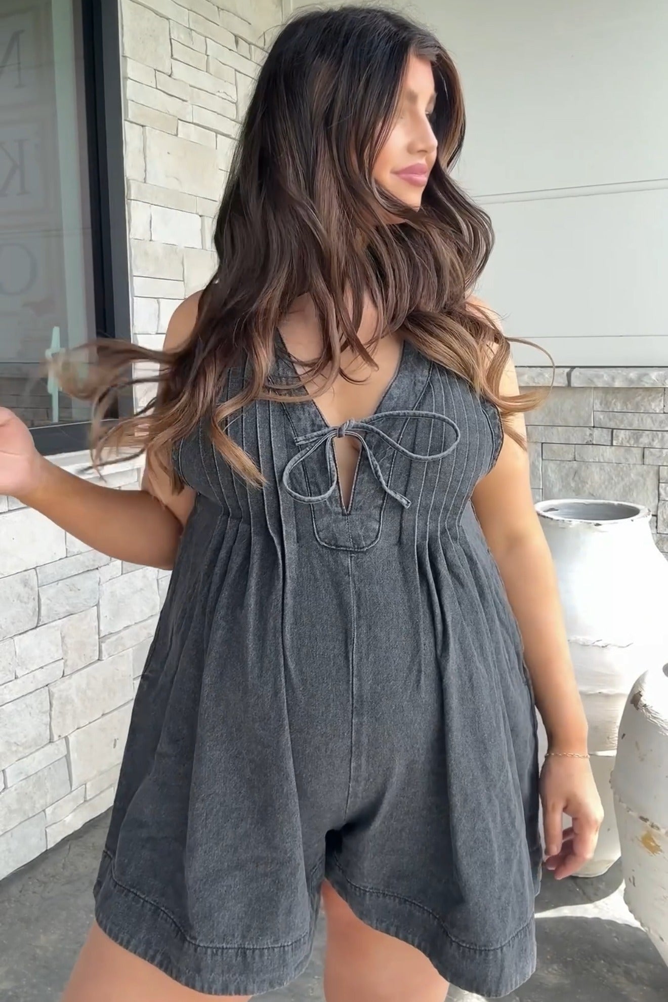 woman wearing a dark gray maternity romper with a tie front and pleat details, showcasing her baby bump