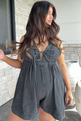 woman wearing a dark gray maternity romper with a tie front and pleat details, showcasing her baby bump