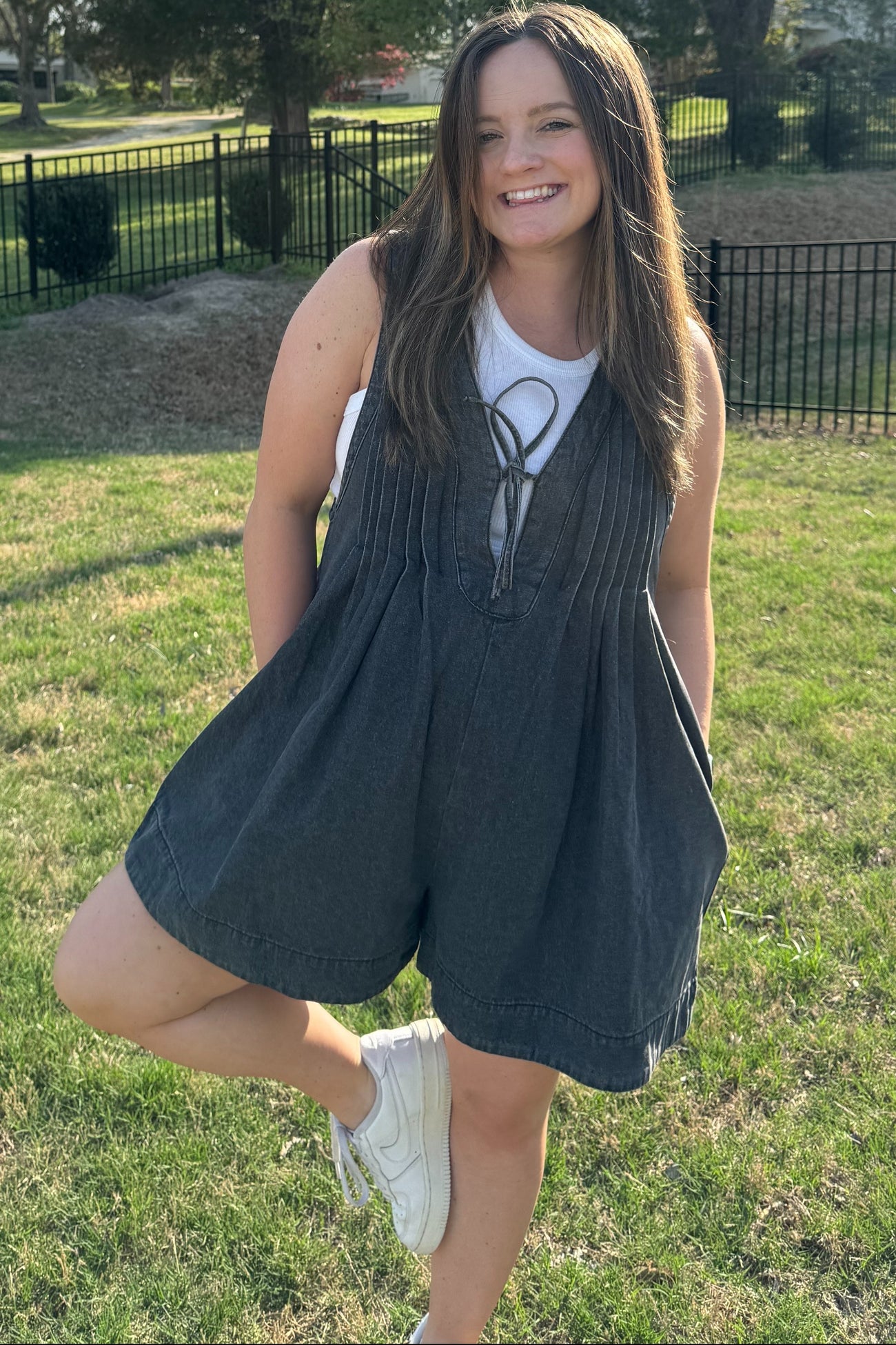 woman wearing a dark denim maternity romper with a front tie detail, smiling outdoors with a grassy background