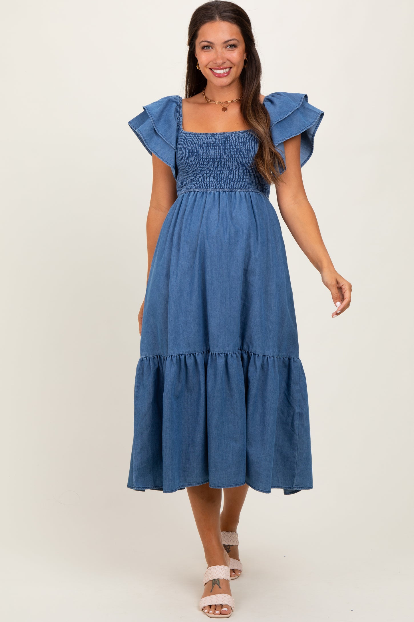 woman wearing a dark denim maternity dress with ruffled sleeves and a tiered hem, smiling at the camera