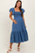 woman wearing a blue denim maternity dress with ruffled sleeves and a smocked bodice, holding her baby bump
