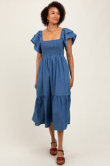 woman wearing a blue chambray midi dress with ruffled sleeves and a tiered skirt
