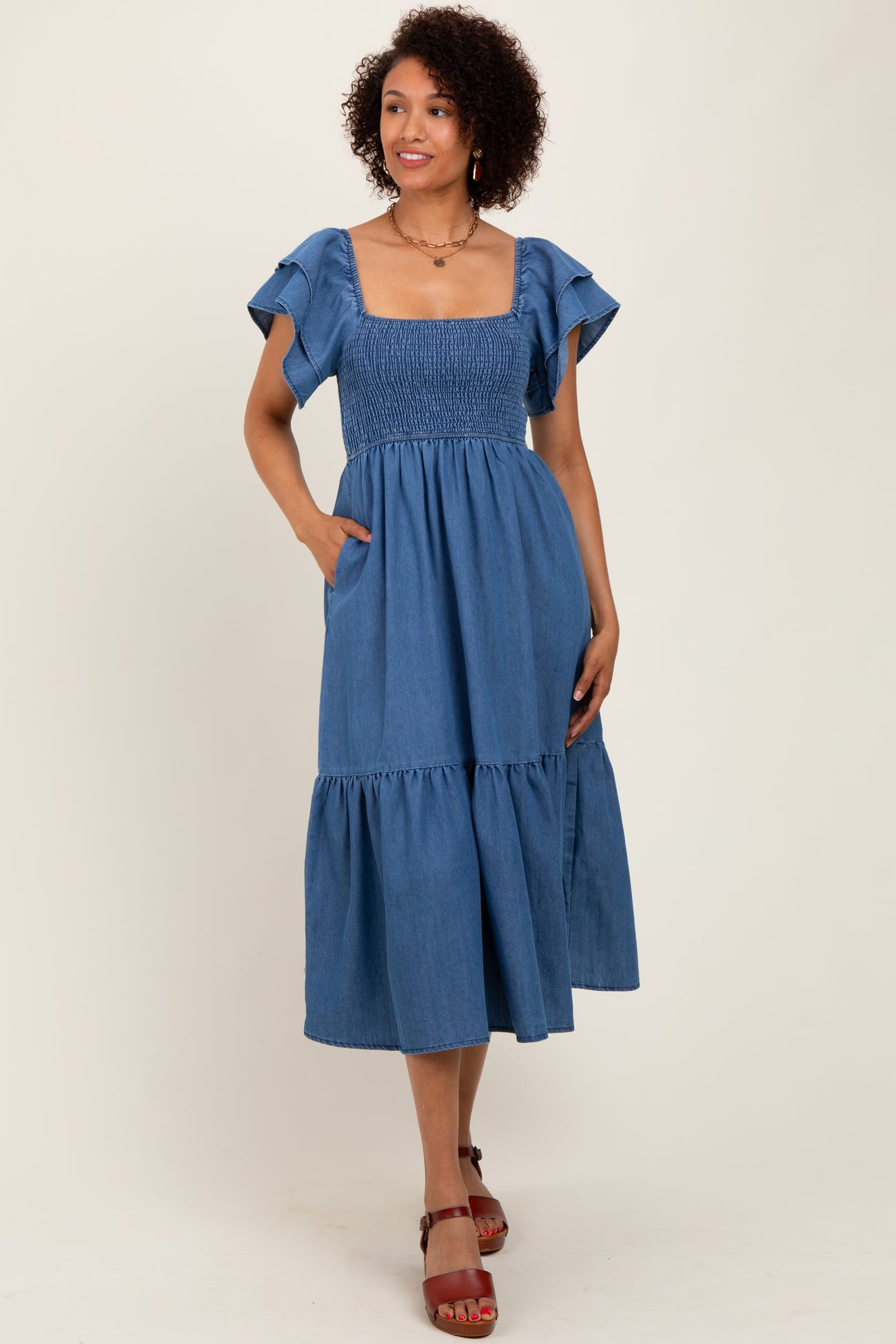 woman wearing a blue chambray midi dress with ruffled sleeves and pockets