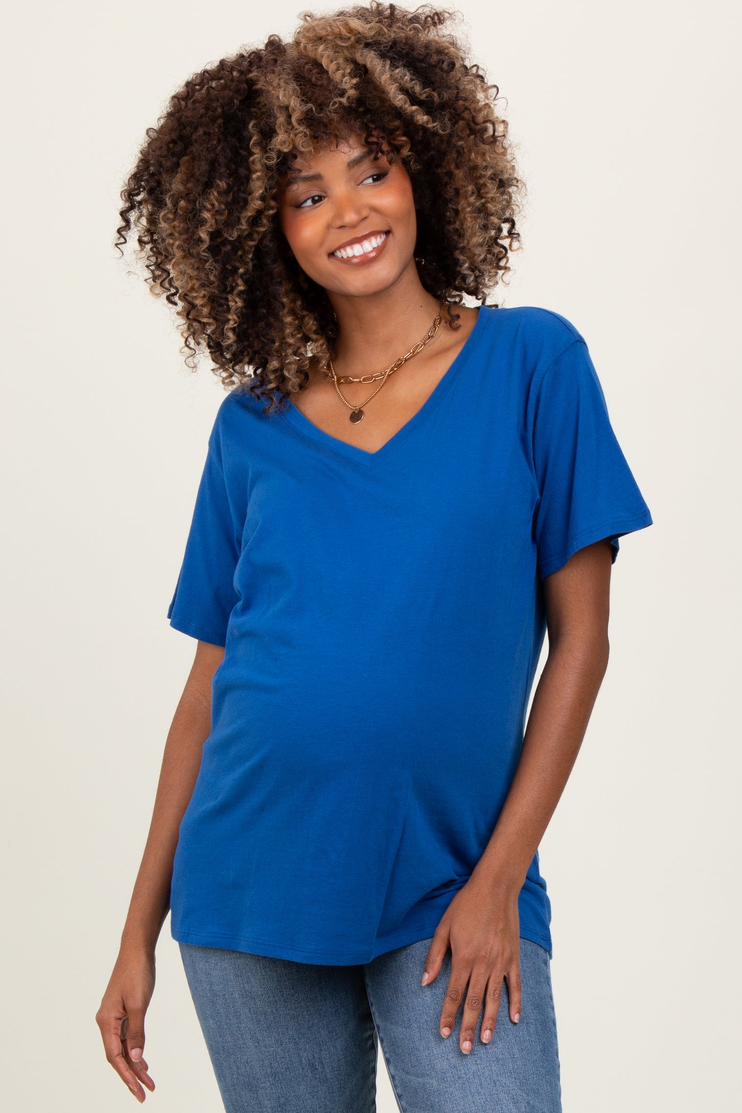 woman wearing a blue v-neck maternity top with a visible baby bump, styled with denim jeans