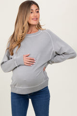 woman wearing a light gray maternity sweatshirt and holding her baby bump while standing in blue jeans