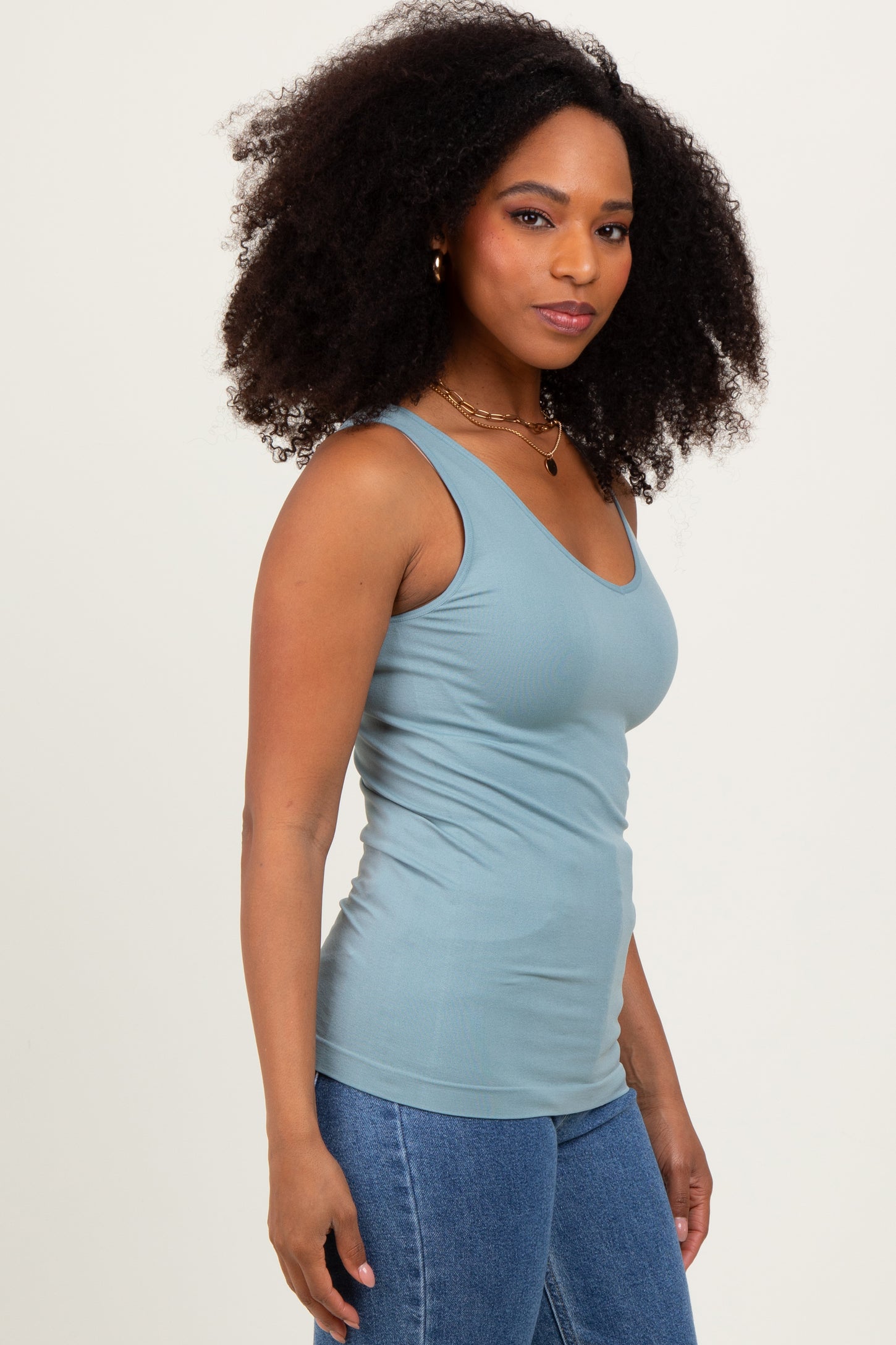 woman wearing a light blue fitted tank top and blue high-waisted jeans with curly hair styled loose