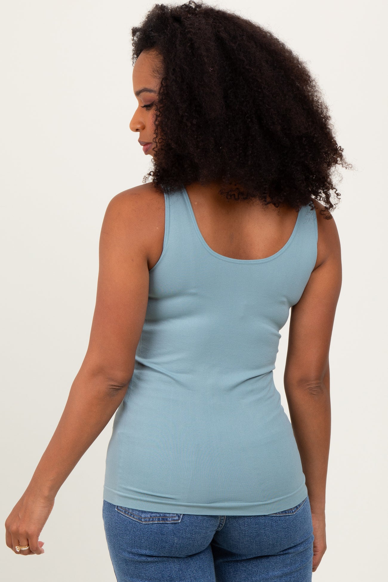 woman wearing a light blue fitted tank top and blue jeans, showing the back view and curly hair