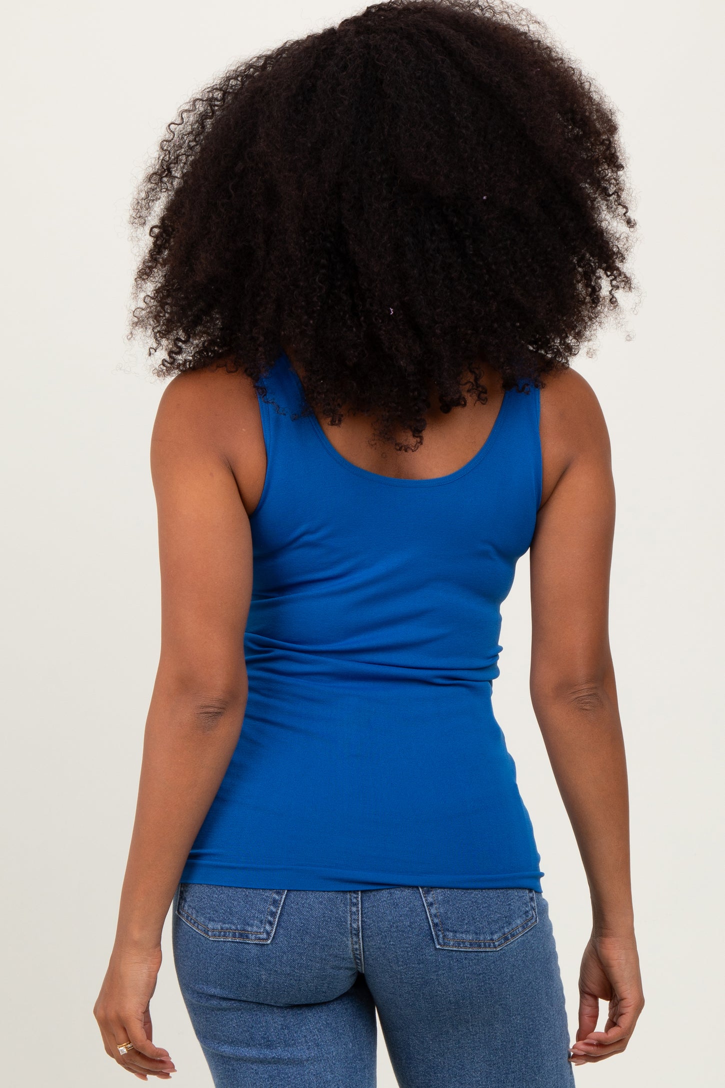 woman wearing a blue fitted tank top with a scoop back and paired with faded blue jeans