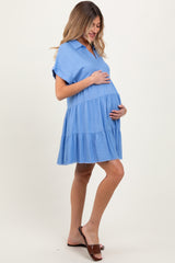 woman wearing a light blue tiered maternity dress, gently cradling her baby bump