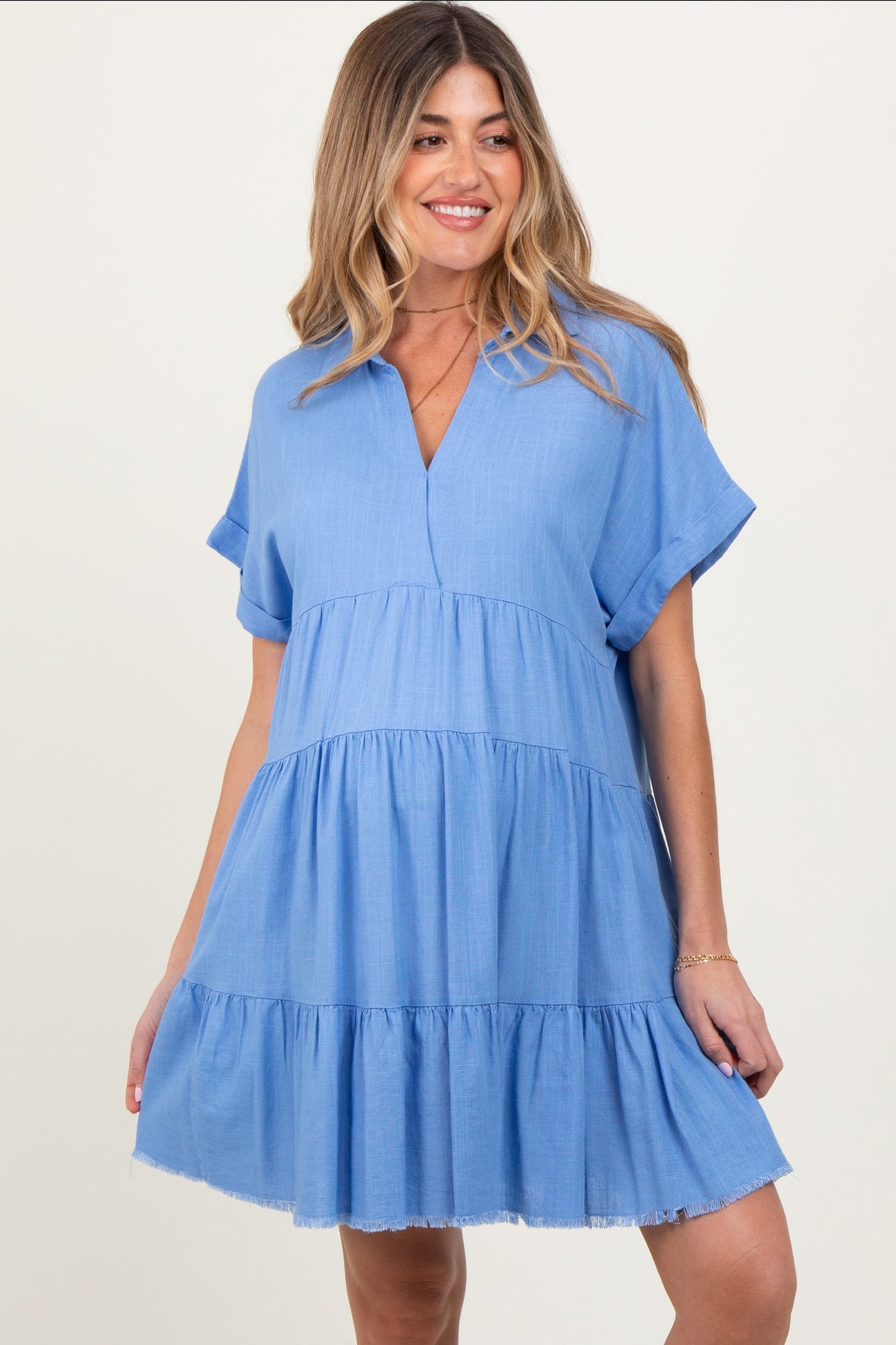 woman wearing a light blue maternity dress with a v-neck and tiered ruffle detail, smiling at the camera