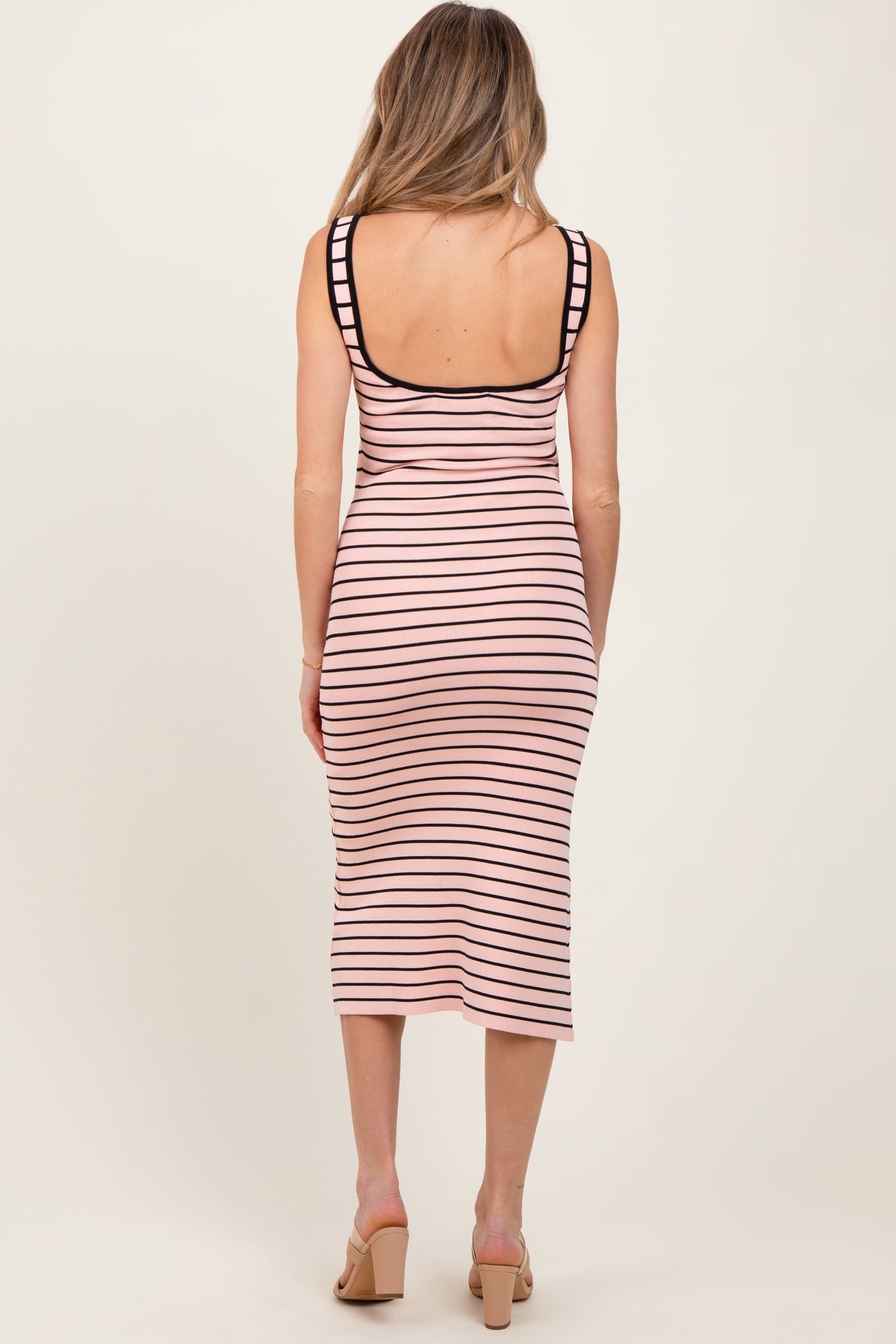 woman wearing a striped pink and black midi maternity dress, showing a fitted silhouette from the back