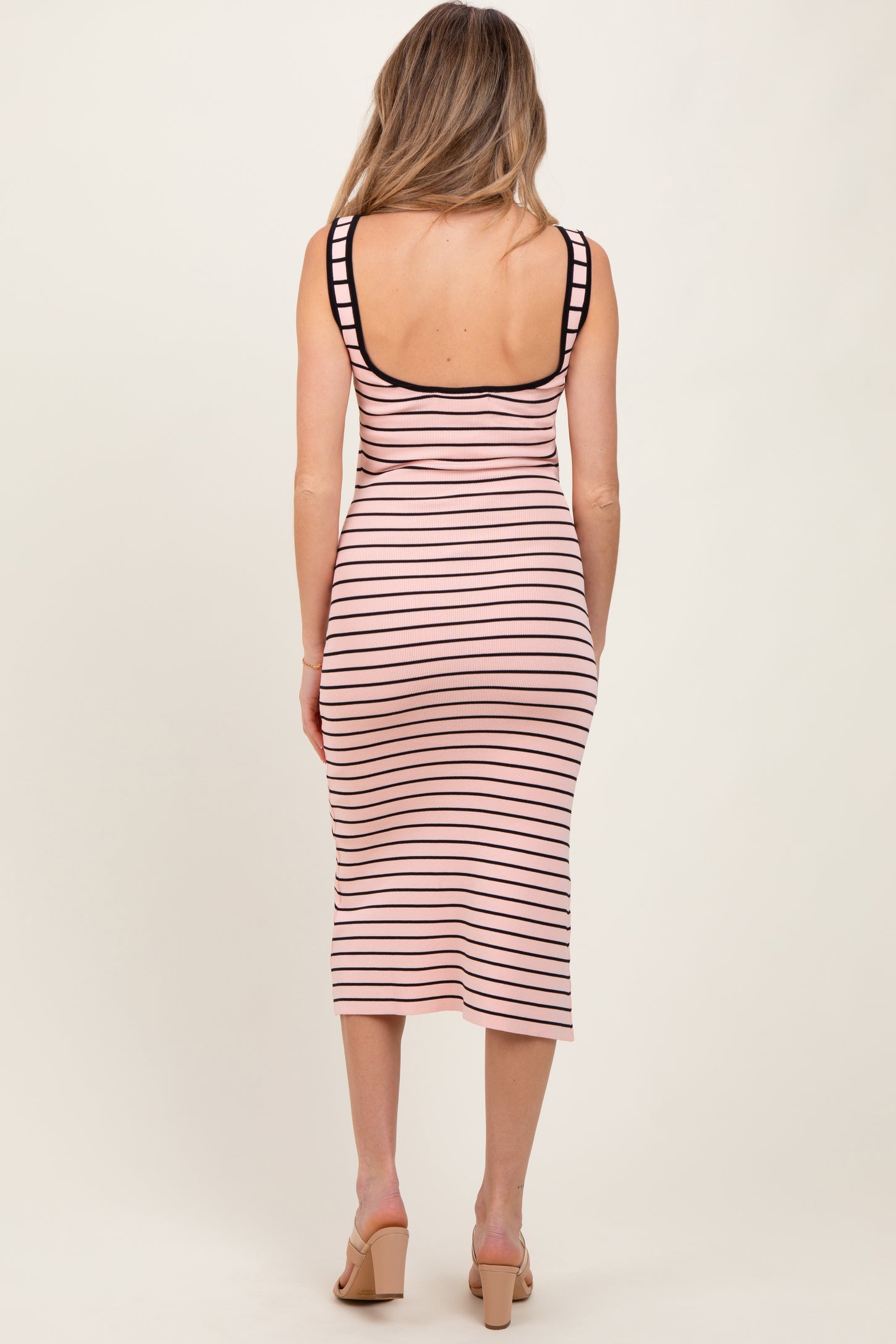 woman wearing a striped pink and black midi maternity dress, showing a fitted silhouette from the back