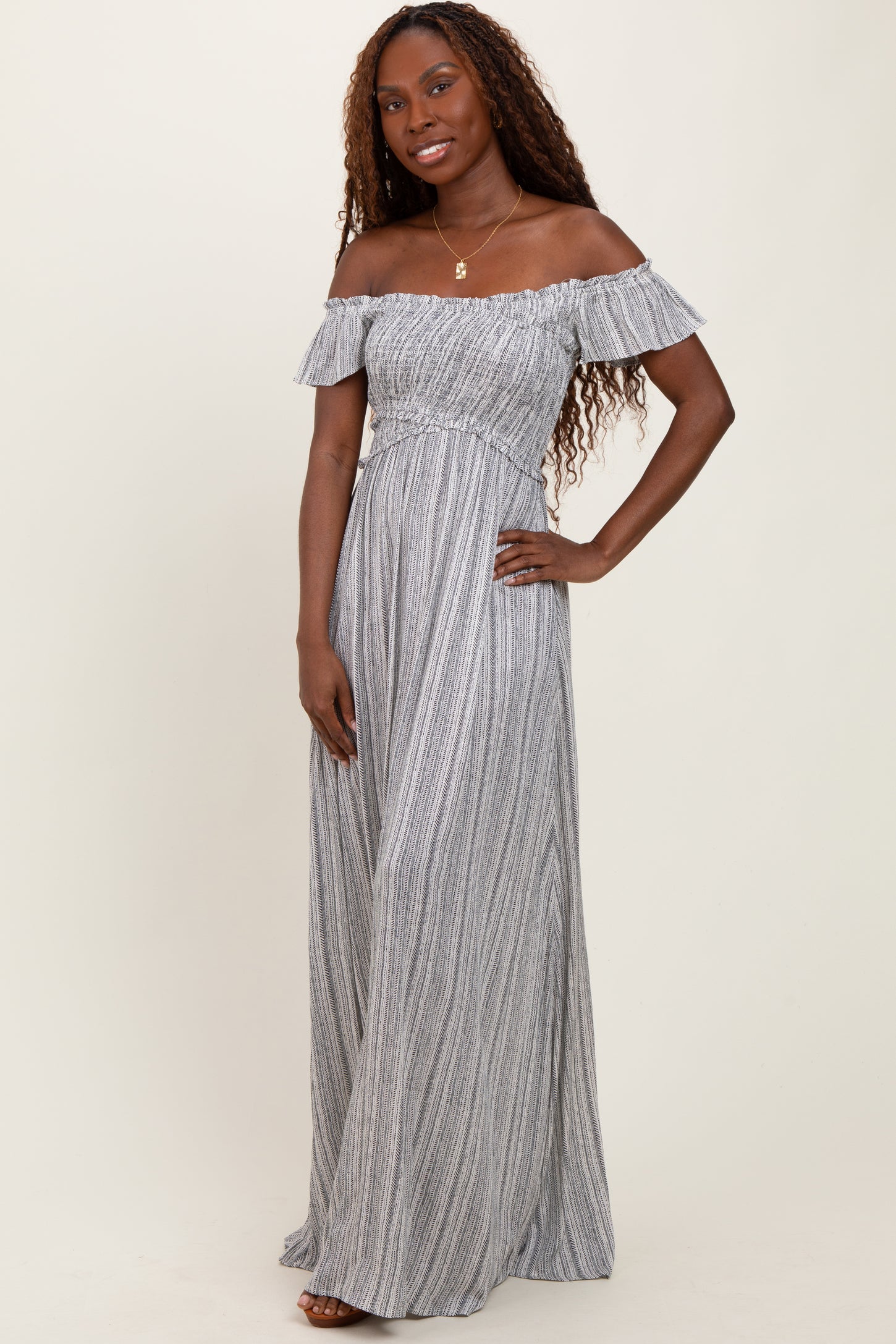 woman wearing a gray and white striped off-the-shoulder maxi dress with ruffle details and a fitted waist