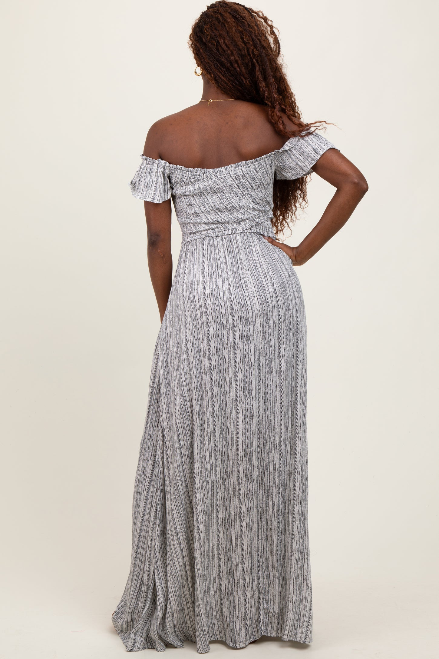 woman wearing a long off-the-shoulder striped maxi dress, showing a fitted bodice and flowing skirt from the back