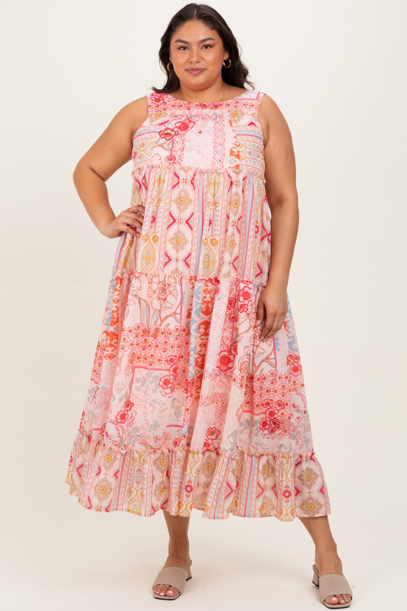woman wearing a colorful plus size maxi dress with a tiered design and floral patterns, standing with one hand on her hip