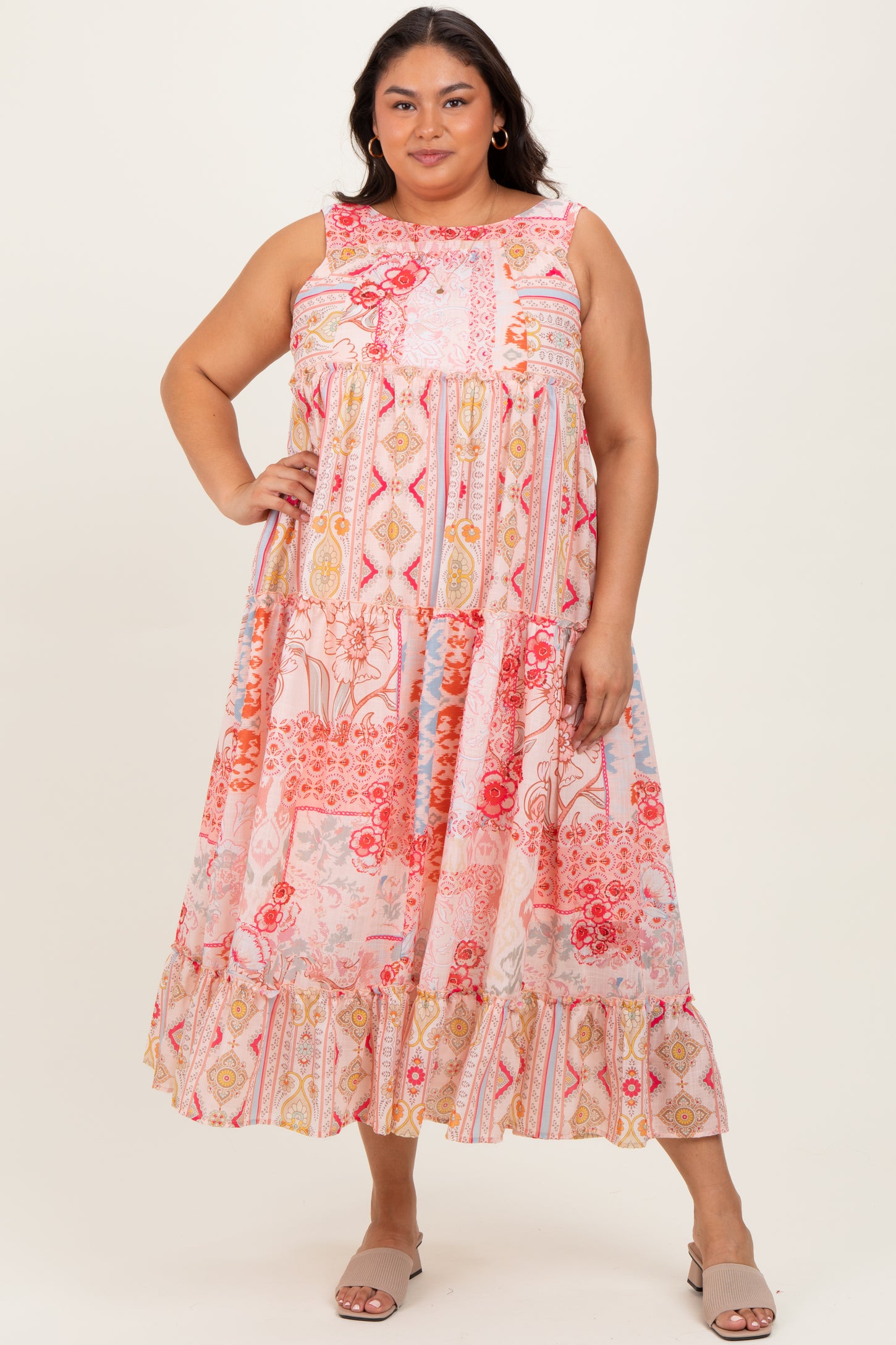 woman wearing a colorful plus size maxi dress with a tiered design and floral patterns, standing with one hand on her hip