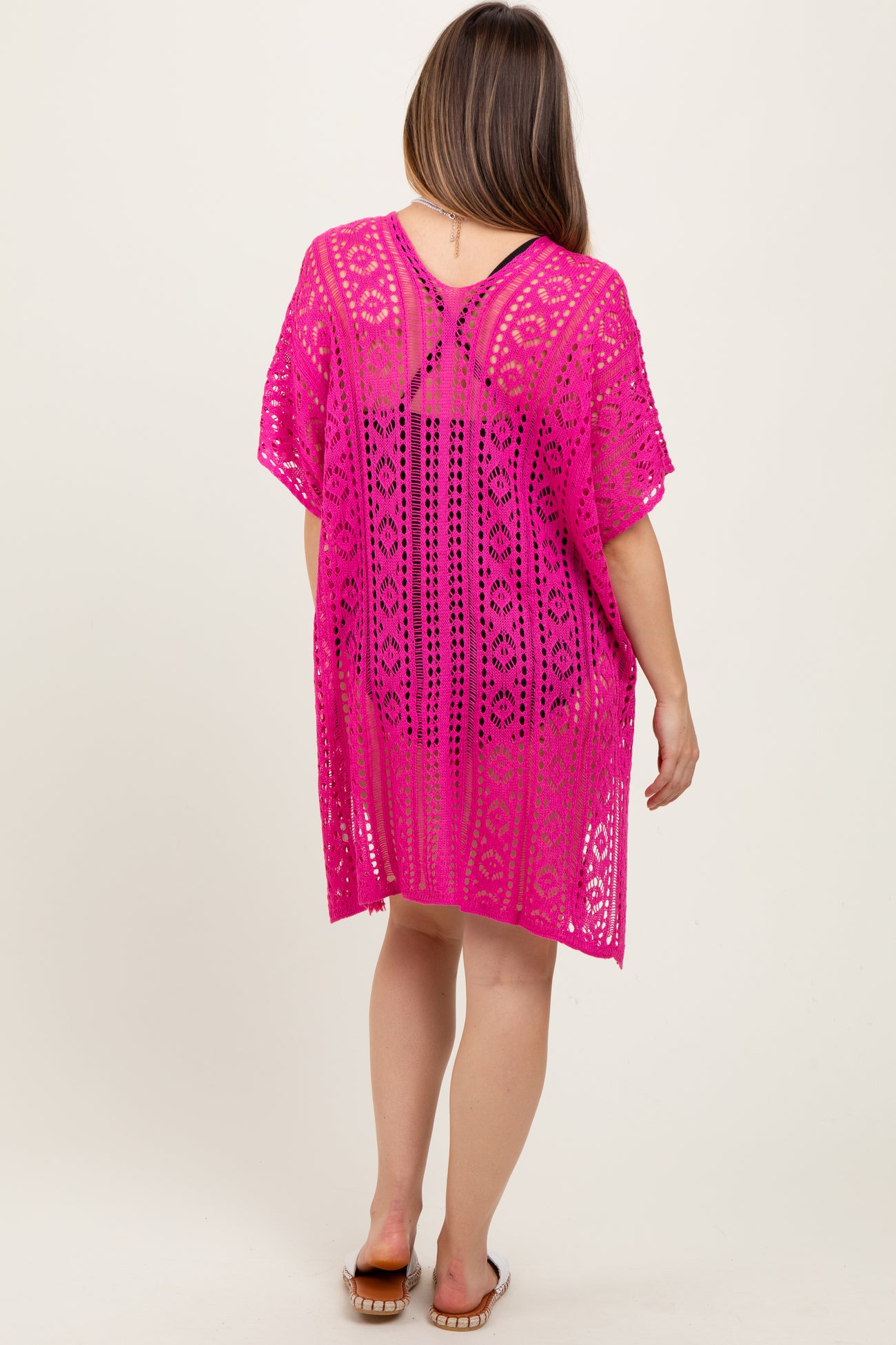 woman wearing a vibrant pink crochet maternity cover-up with an open back, showing a relaxed fit and intricate pattern