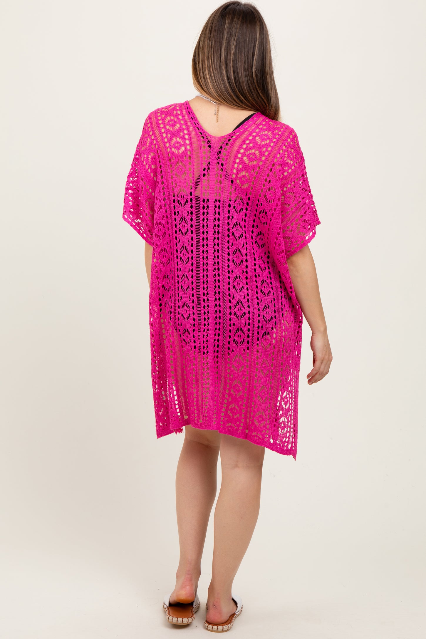 woman wearing a vibrant pink crochet maternity cover-up with an open back, showing a relaxed fit and intricate pattern