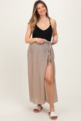 woman wearing a black ribbed maternity tank top and a beige maxi skirt with a tie waist and side slit