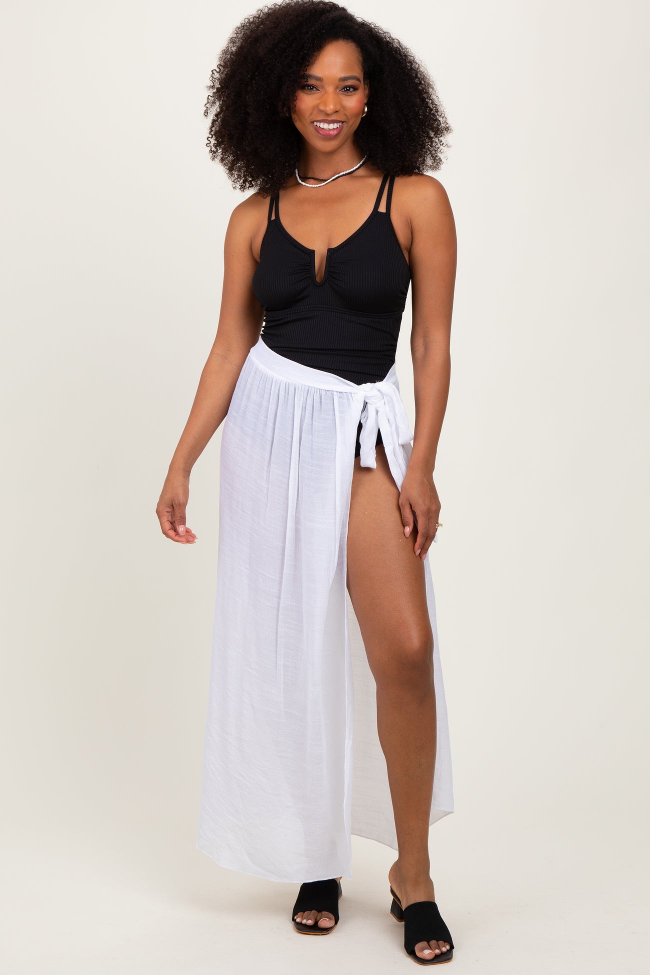 woman wearing a black ribbed swimsuit top and a white maxi wrap skirt, posing with one hand on her hip