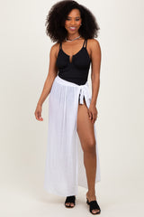 woman wearing a black ribbed swimsuit top and a white maxi wrap skirt, posing with one hand on her hip