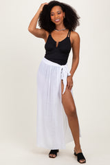 woman wearing a black ribbed bikini top and a white maxi skirt with a high slit and tie waist detail