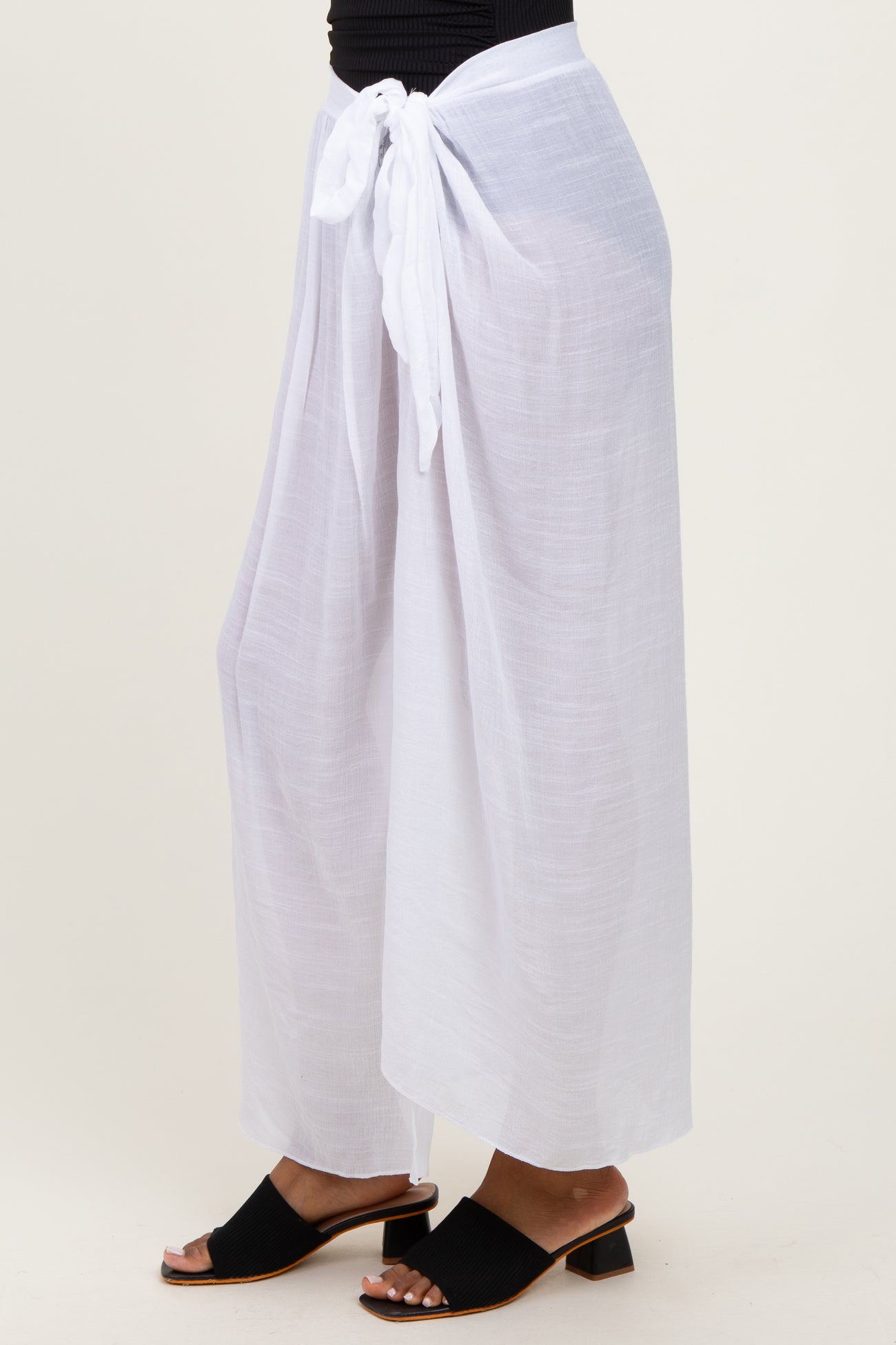 woman wearing white lightweight wide-leg pants tied at the waist with a sash, paired with black slide sandals