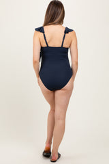 woman wearing a navy blue maternity swimsuit with ruffled straps, showing the back view and no visible baby bump