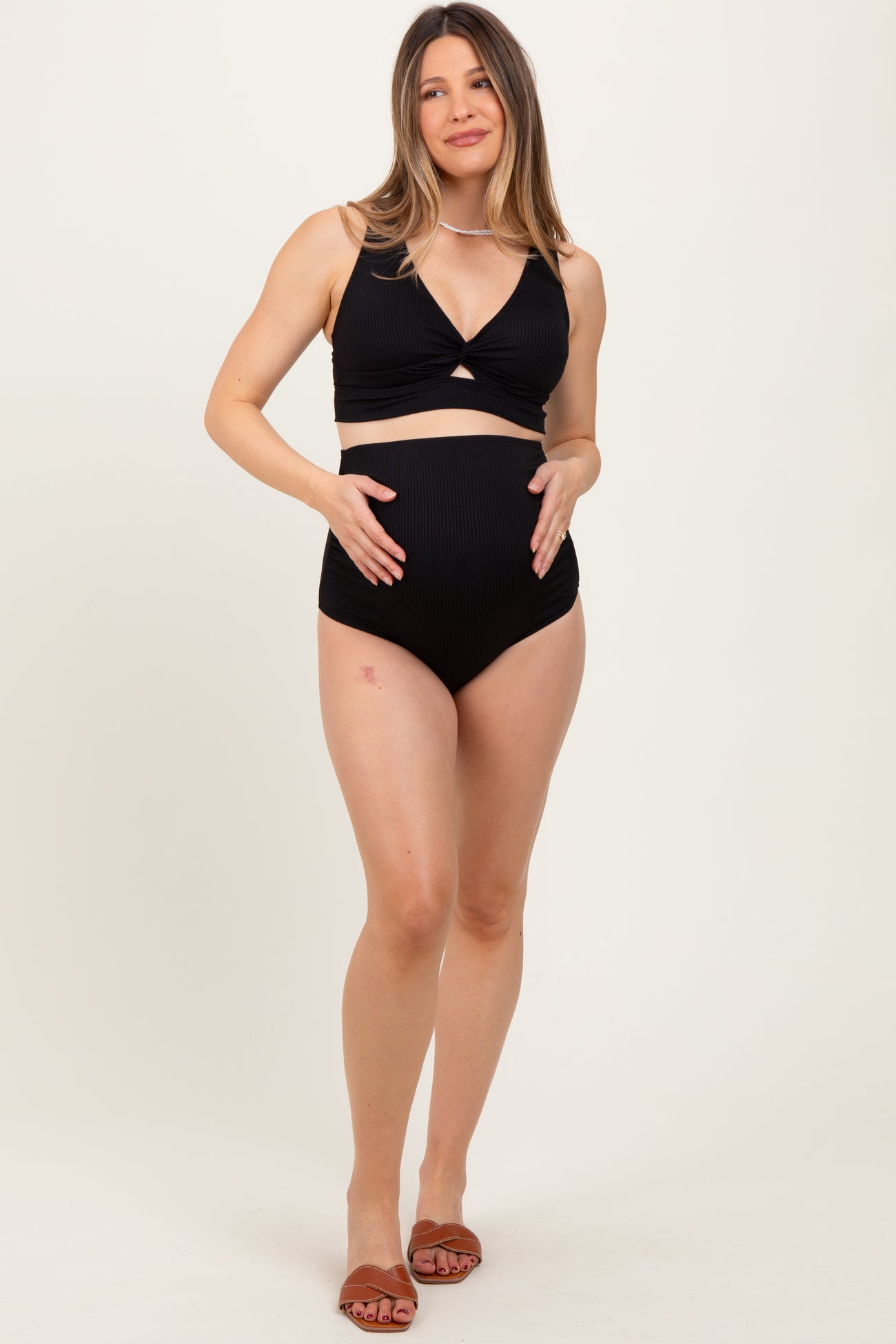 woman wearing a black ribbed maternity bikini top and high-waisted bottom, holding her baby bump