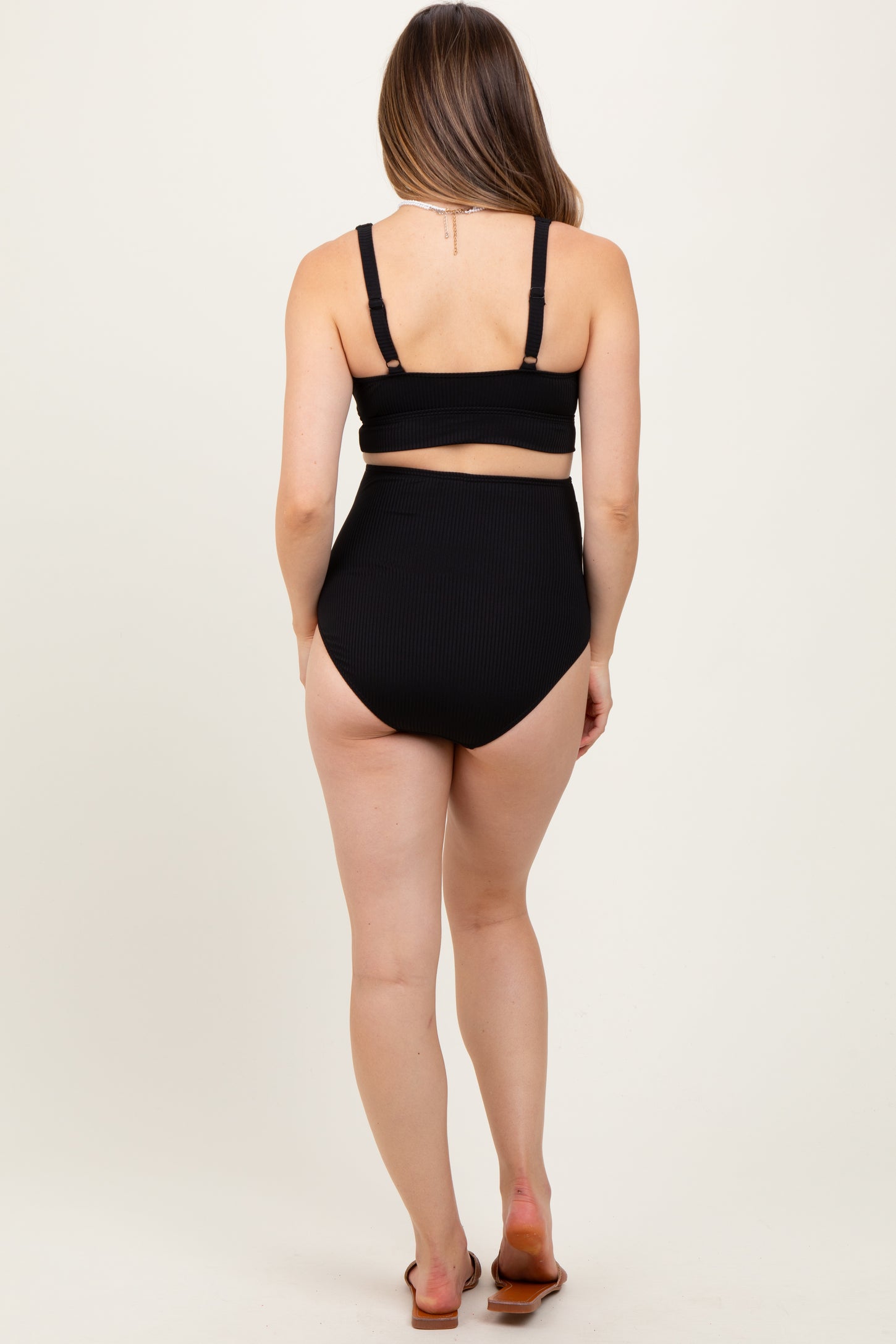 woman wearing a black ribbed maternity bikini top and high-waisted bottom, showing her back and no visible baby bump