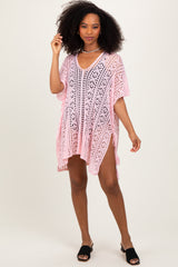 woman wearing a pink crochet cover-up with short sleeves and a v-neckline, standing and posing stylishly