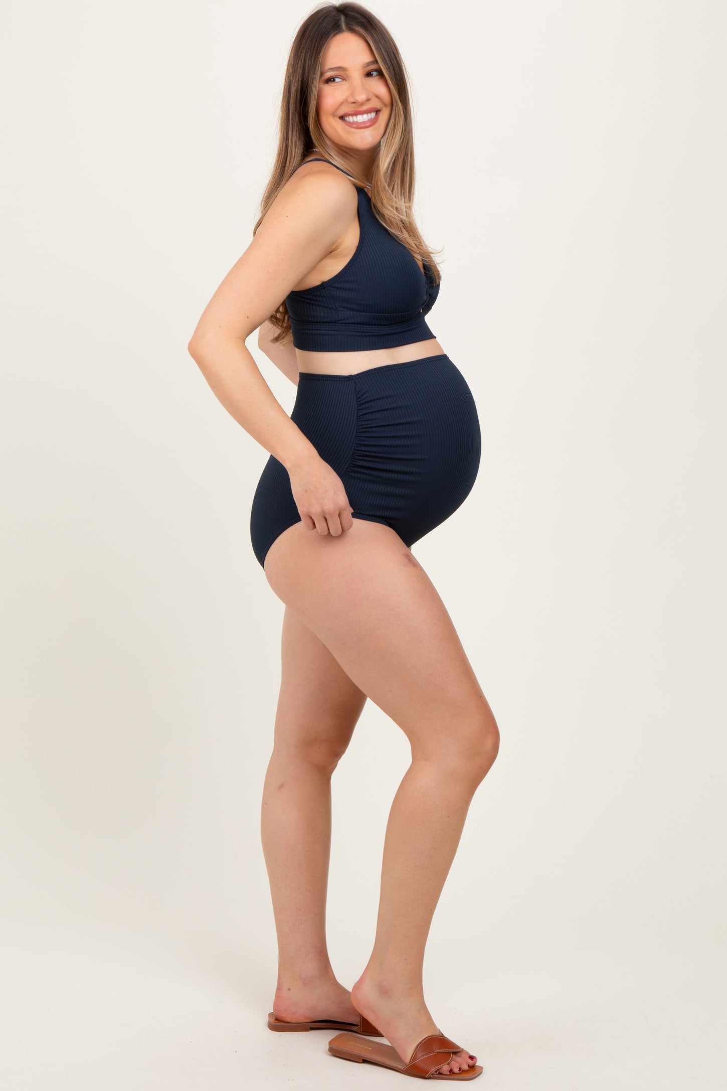 woman wearing a navy blue maternity bikini set with a supportive top and high-waisted bottoms, showing her baby bump